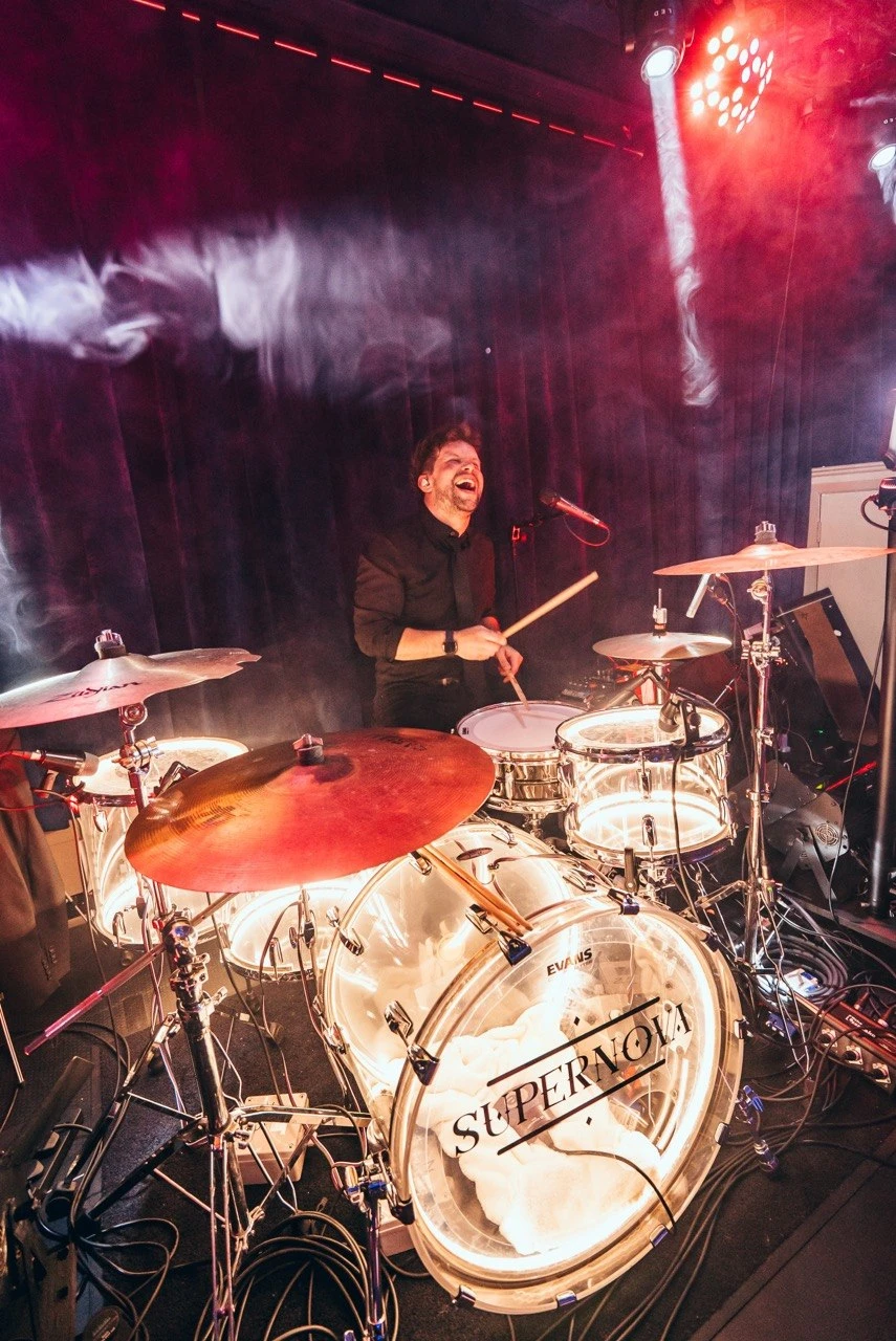 Callum behind the Supernova branded drum kit with haze and stage lights