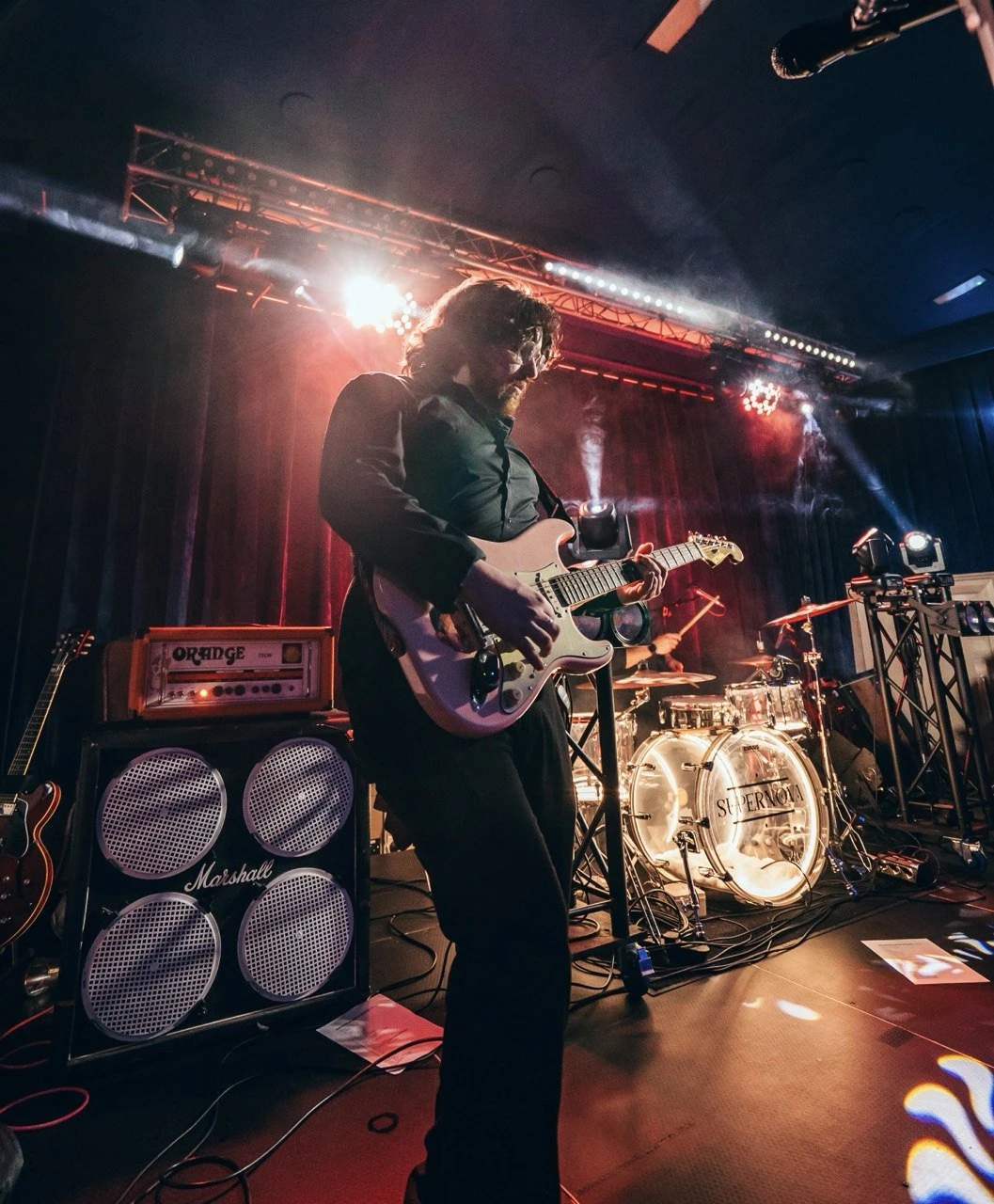 Guitarist silhouette with Orange amp, Marshall cab and lit drum kit